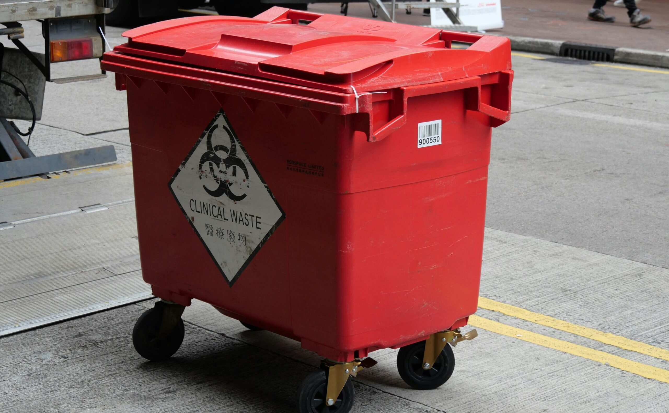 A red clinical waste bin labeled with biohazard symbol on a city street indicating proper waste management.