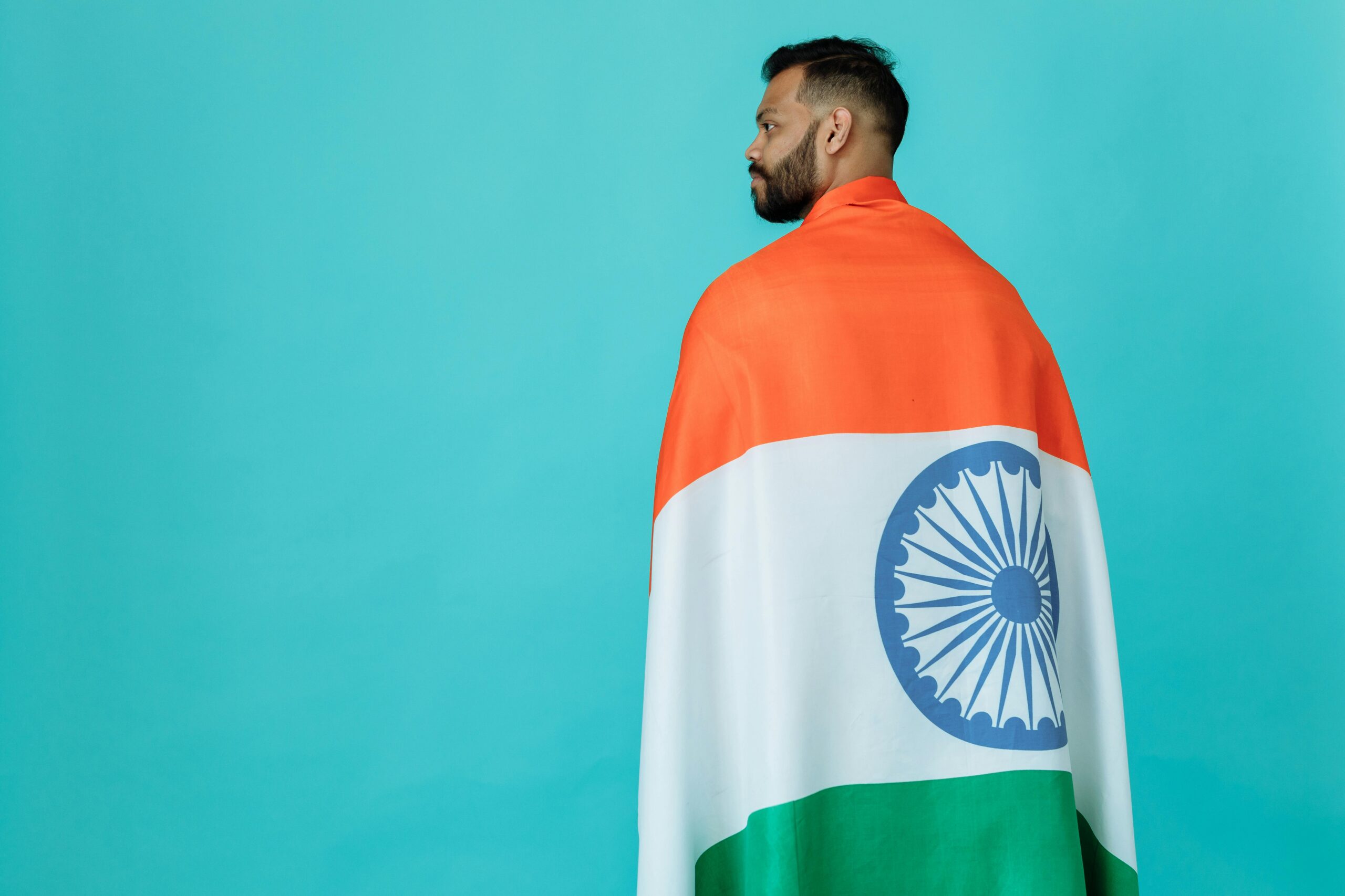 Man draped in Indian flag against turquoise backdrop symbolizing patriotism and pride.